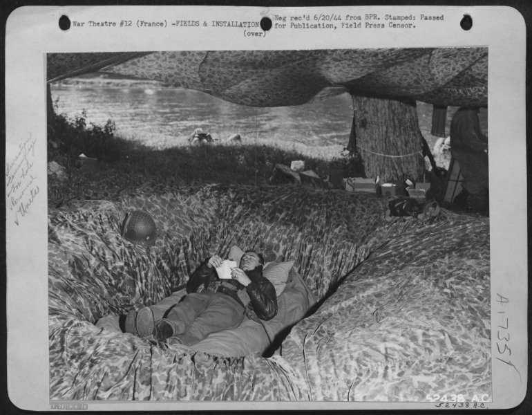 Maj. James T. Nelson, of the 101st Airborne Division of the 9th AF reads in a camouflaged foxhole, an effect made by parachute silk – National Archives Identifier: 204891532